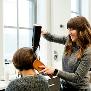 A stylist blow-drying a client in the chair
